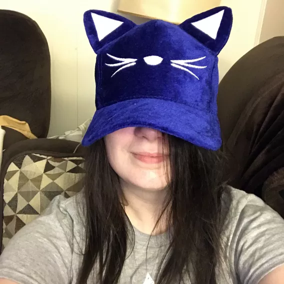 Woman with dark hair, having her face partially obscured by a blue hat that has cat ears.